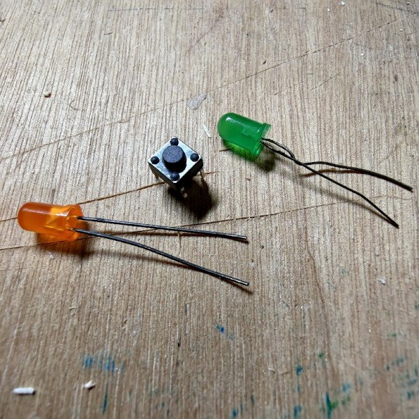 A momentary switch, an orange LED and a green LED on a wooden table